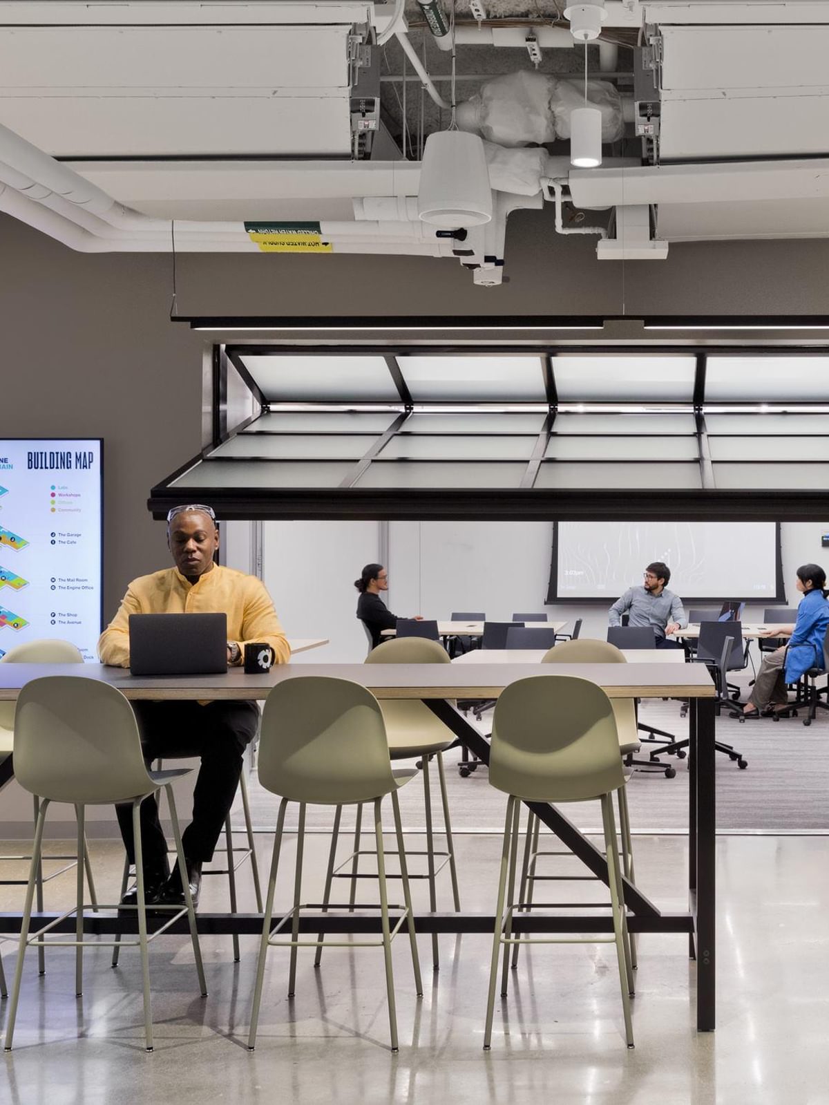 A Tough Tech resident works at a laptop on a table in The Engine's open shared workspace.